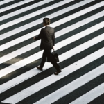 Process & Systems Review man in black formal suit jacket and pants carrying black bag while walking on pedestrian lane during daytime