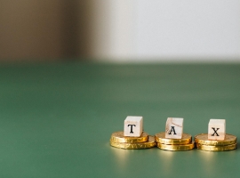 Stacked gold coins with wooden blocks spelling 'TAX' on a green backdrop.