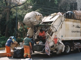 Street workers in Mexico City loading garbage truck during daytime.