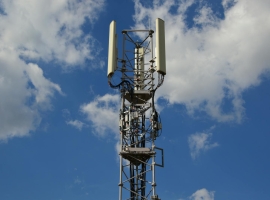 A tall cellular communication tower against a vivid blue sky, symbolizing modern technology.