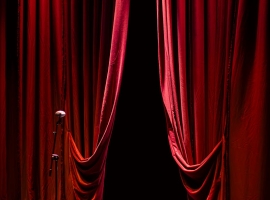 A theater stage with closed red curtains and a single microphone in the spotlight, creating a dramatic ambiance.