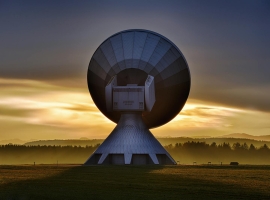 Large satellite dish silhouette against a colorful sunset, showcasing broadcasting technology.