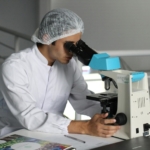 Starting a Pharmaceutical Manufacturing Business in Nigeria Scientist in a lab coat using a microscope to conduct research, focusing on healthcare improvements.