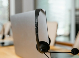 A headset hanging on a computer in a modern office setting for customer support.
