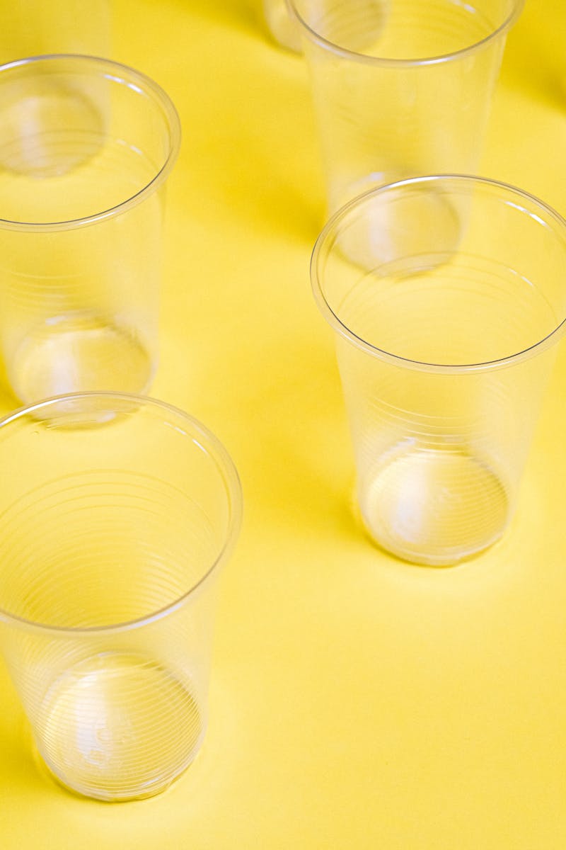 Several transparent plastic cups arranged on a vibrant yellow surface, creating a clean and minimalist composition.