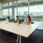 Contemporary office setting with professionals working on laptops at a shared desk.
