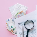 A collection of financial papers, including euro notes, tax return forms, and receipts on a pink surface.