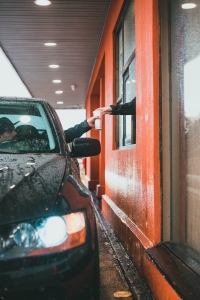 A car receiving a drink from a restaurant drive-through window on a rainy day.