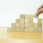 A person placing a block into a pile of wooden blocks
