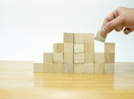 A person placing a block into a pile of wooden blocks